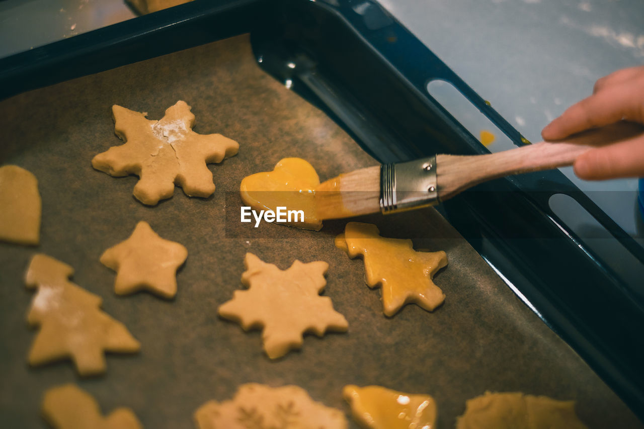 Child coating christmas cookies on a baking sheet with egg yolk.