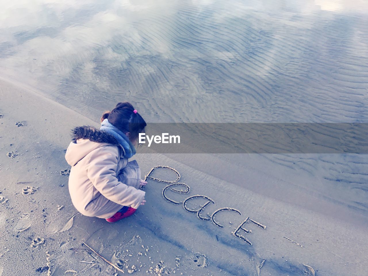 High angle view of girl writing peace text on shore at beach