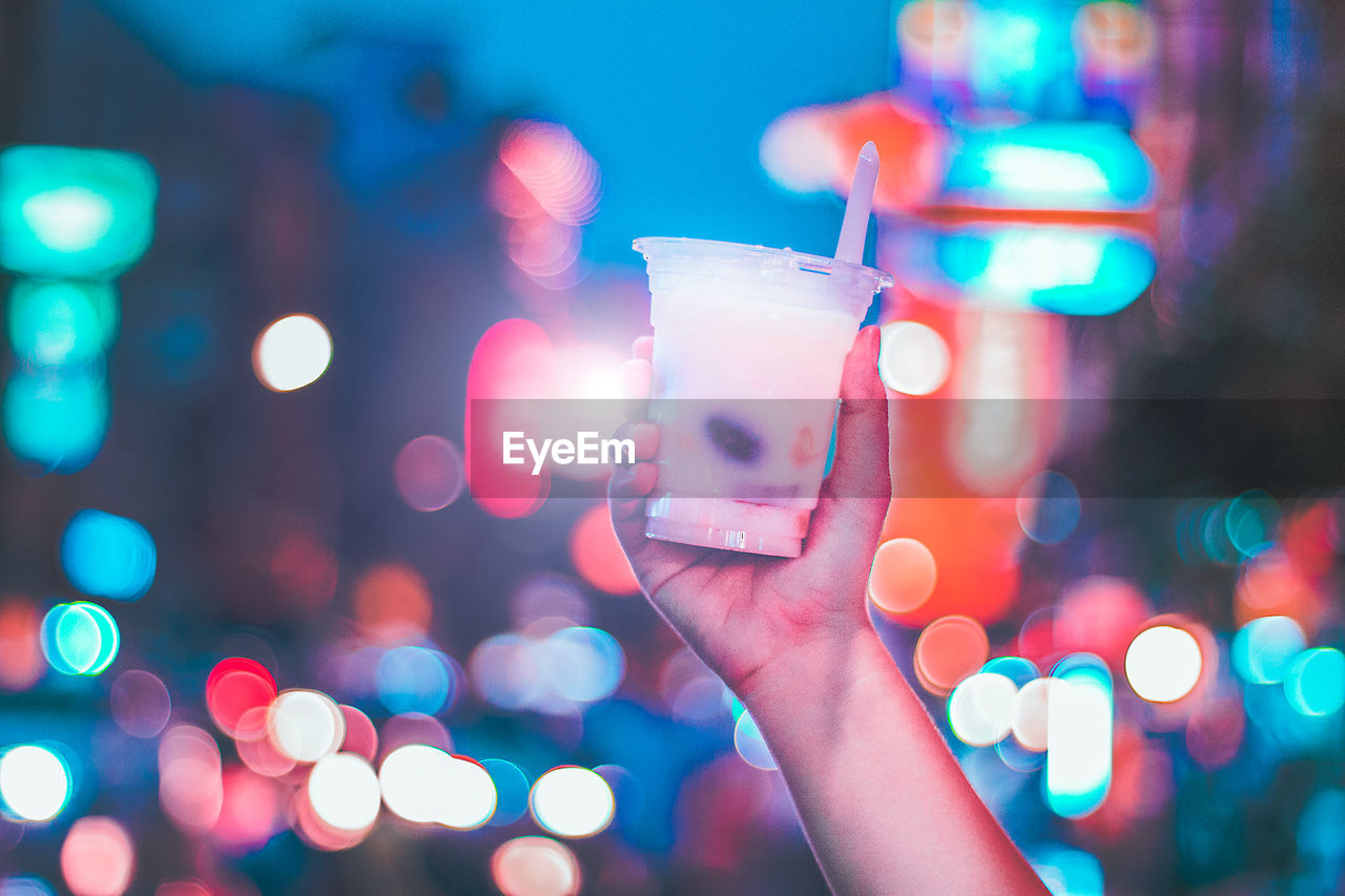 Cropped hand holding drink against illuminated background