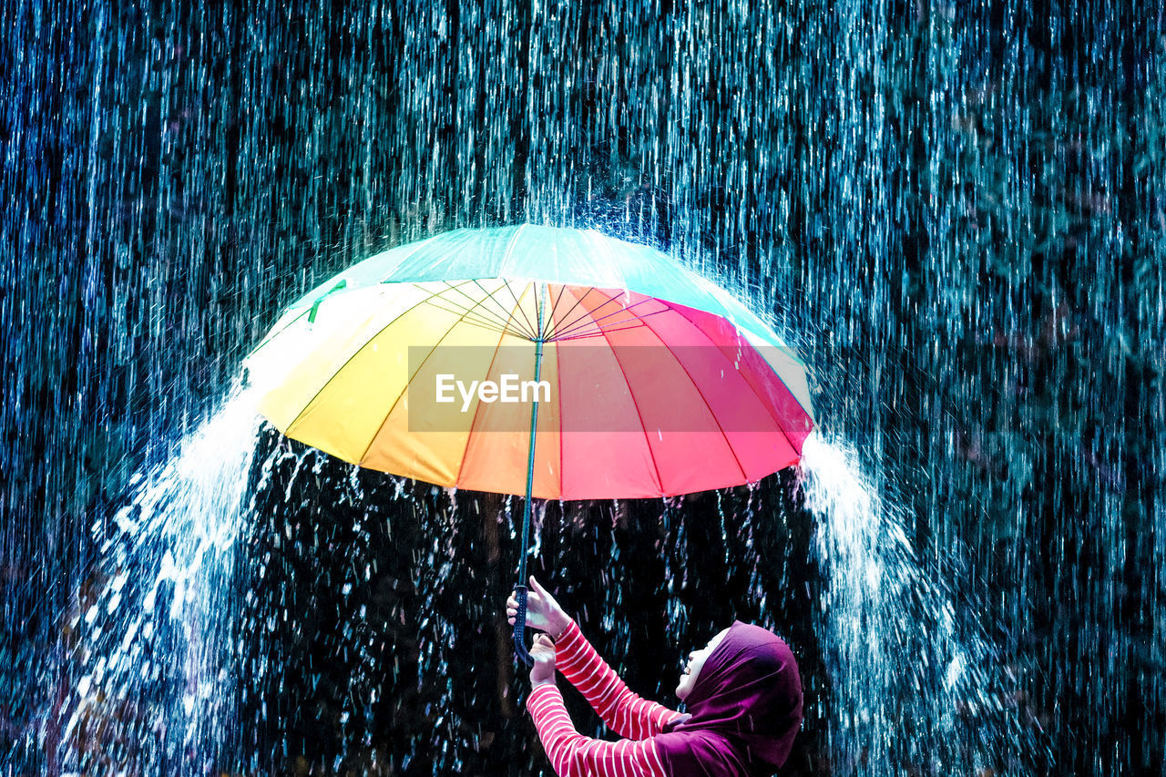 Teenage girl holding colorful umbrella while standing in rain