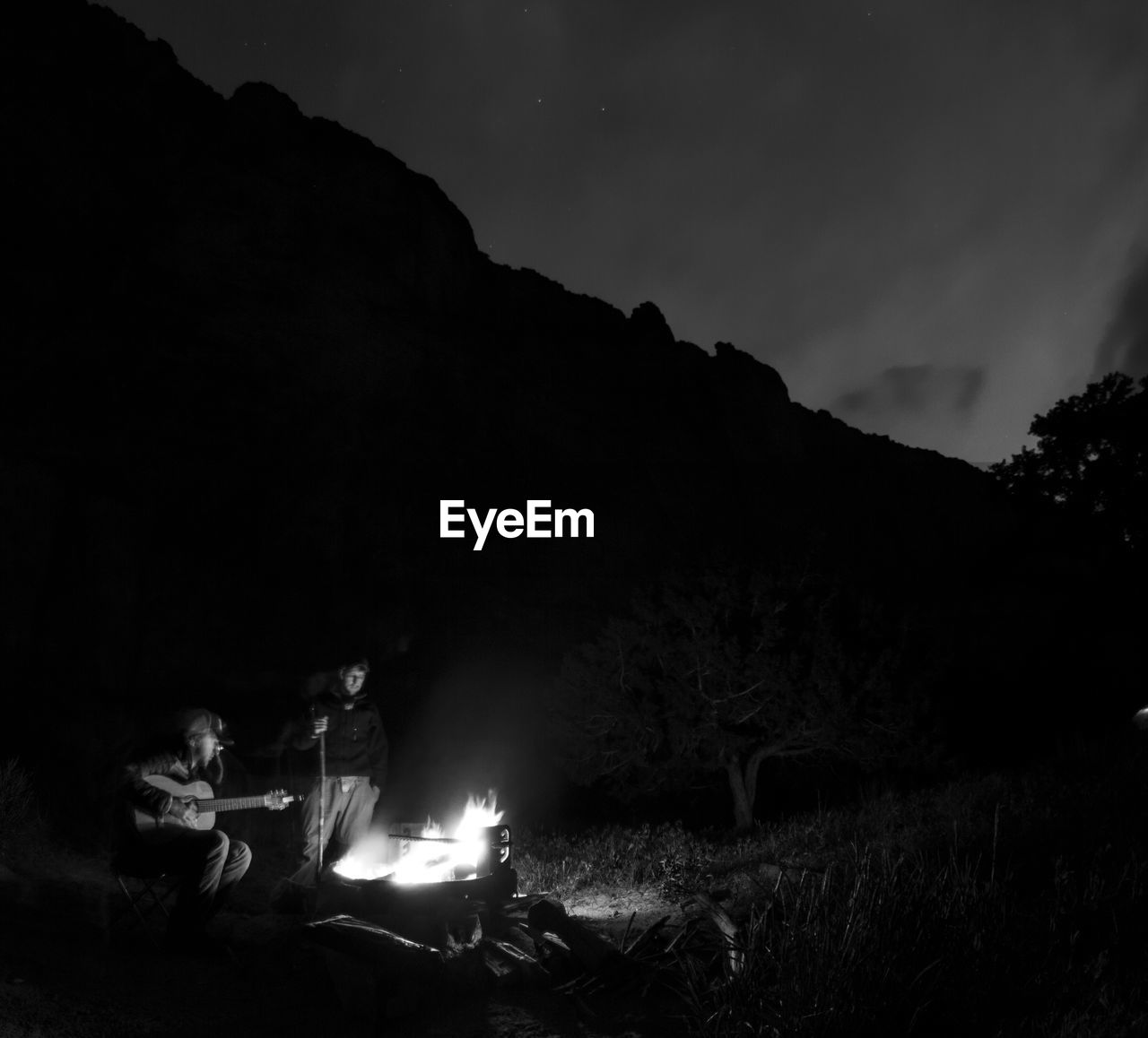 Men by campfire in forest at night