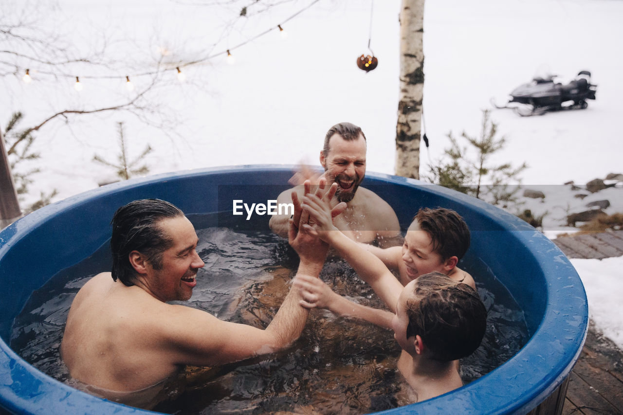 Cheerful mature men and boys giving high-five to each other while taking bath in hot tub