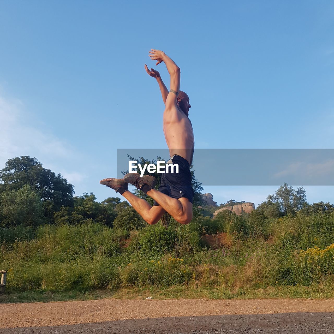 Full length of shirtless man jumping against sky