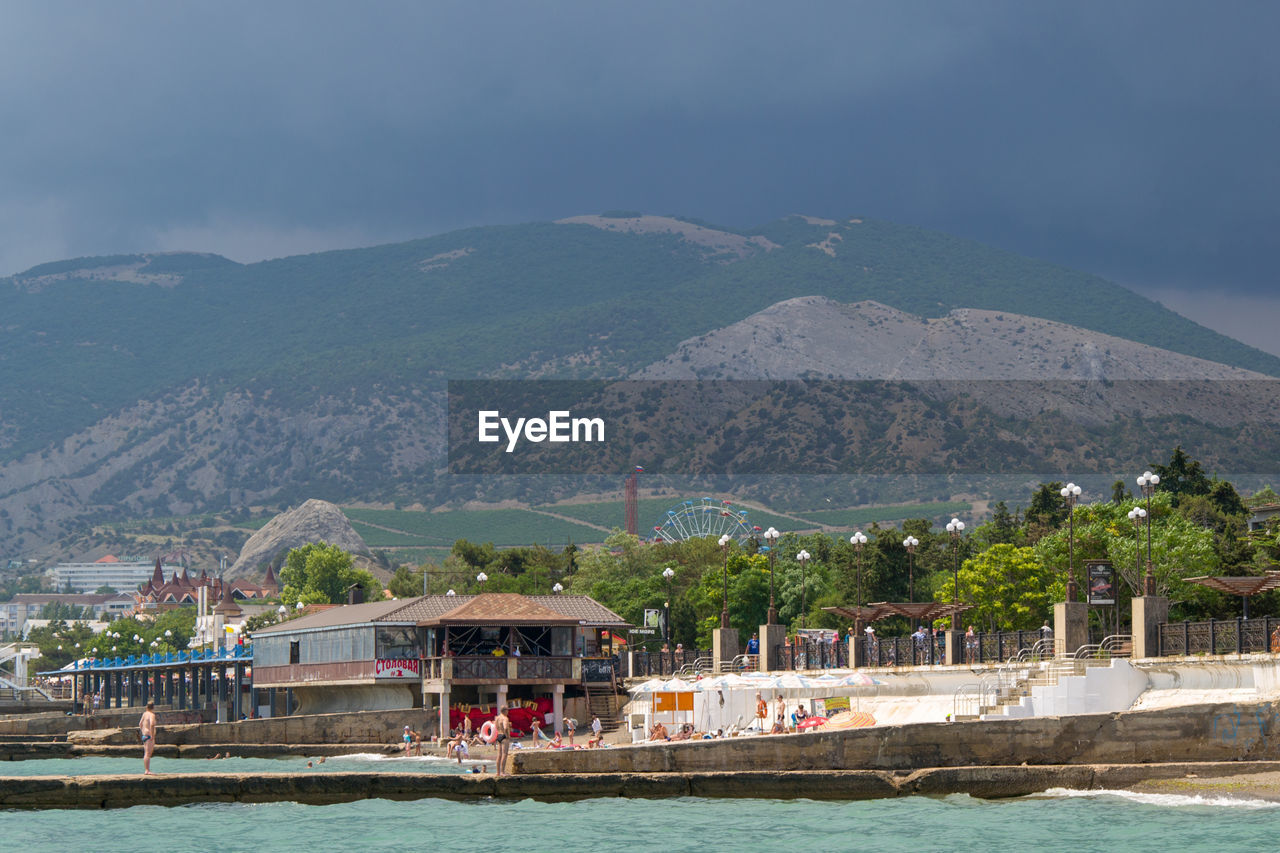 SCENIC VIEW OF SEA AND BUILDINGS AGAINST MOUNTAIN RANGE