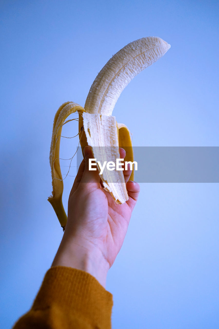 Close-up of hand holding banana against blue background