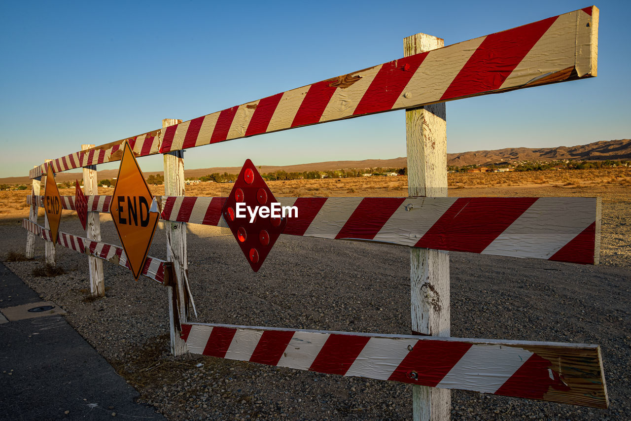 End of paved road barrier with red and white stripes and reflectors and signs in desert