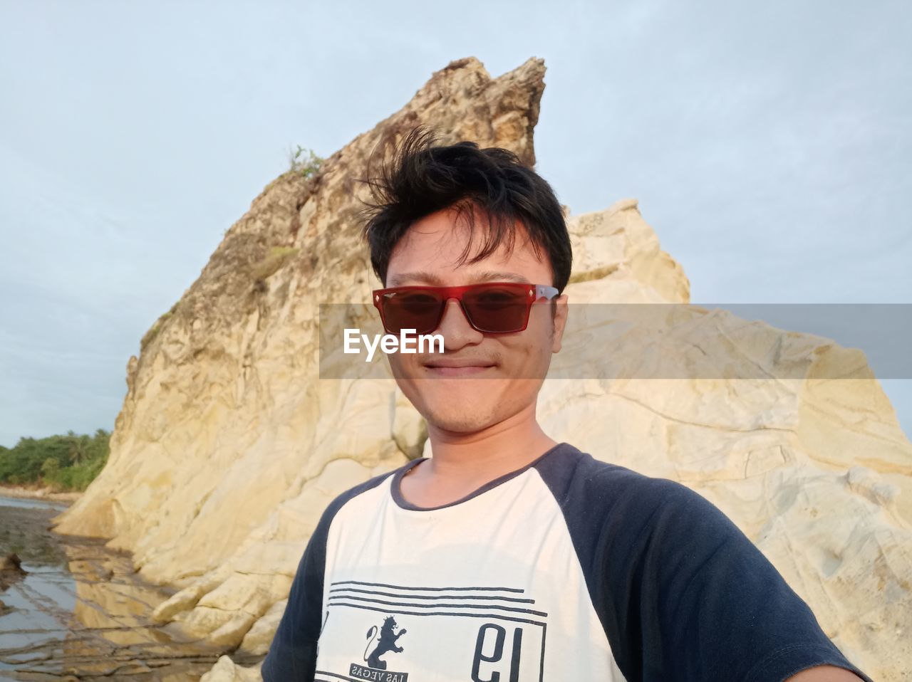 PORTRAIT OF SMILING YOUNG MAN WEARING SUNGLASSES AGAINST SKY