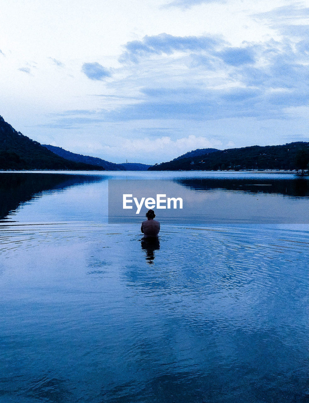 Rear view of man in lake against sky during sunset