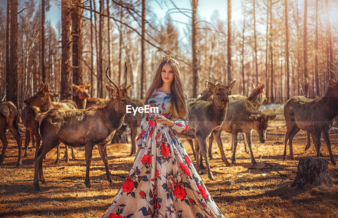 Portrait of young woman standing against deer at forest