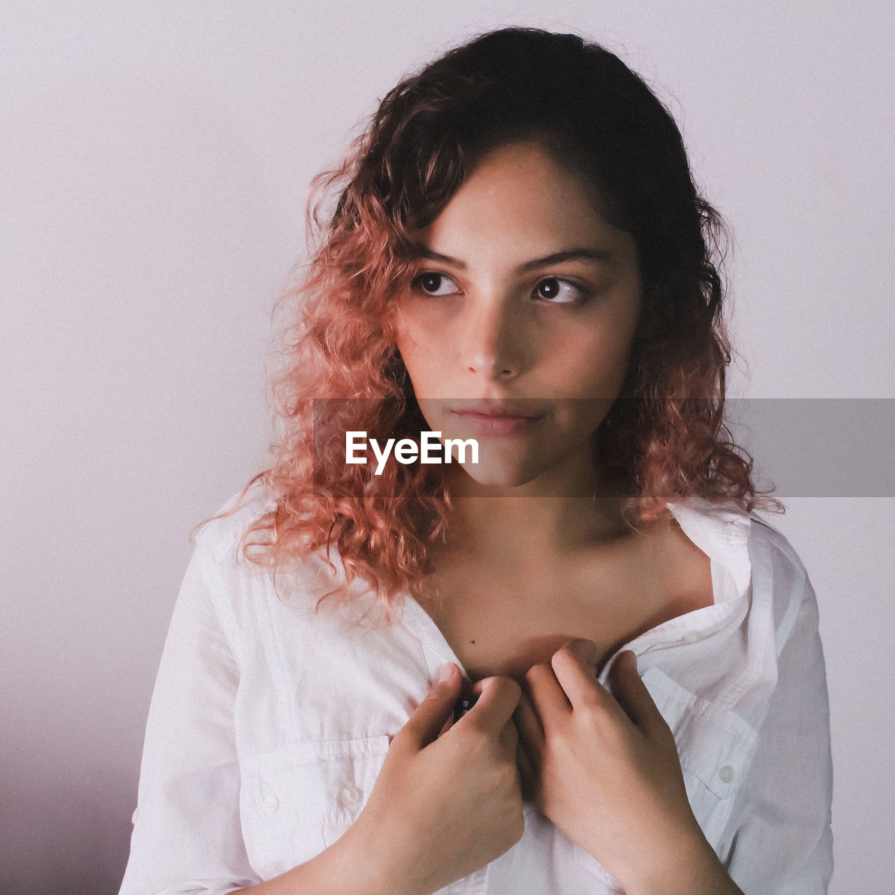 PORTRAIT OF YOUNG WOMAN STANDING AGAINST WHITE BACKGROUND