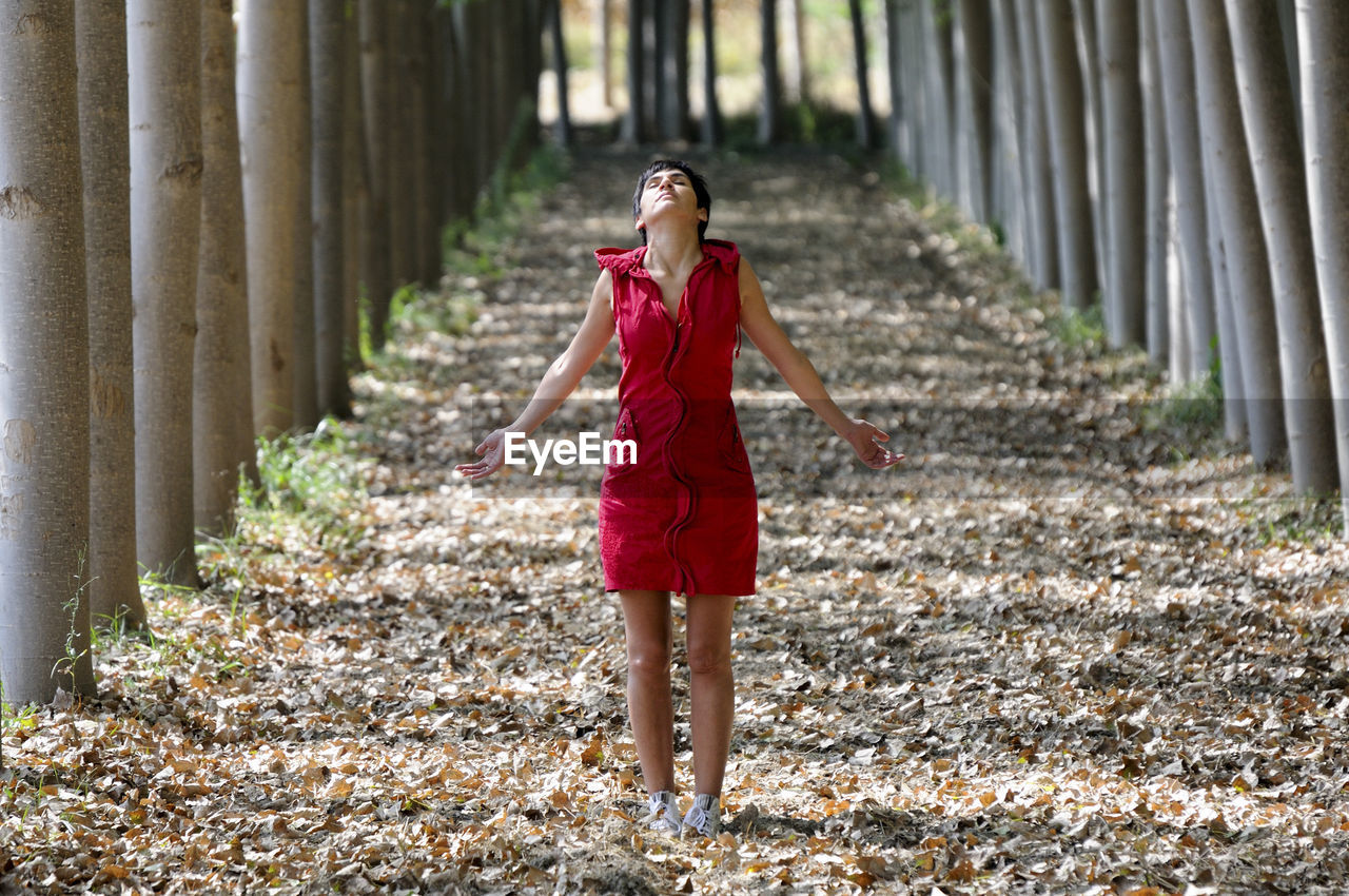 Full length of young woman standing on footpath amidst trees