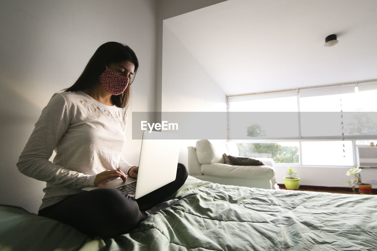 Man using laptop while sitting on bed at home