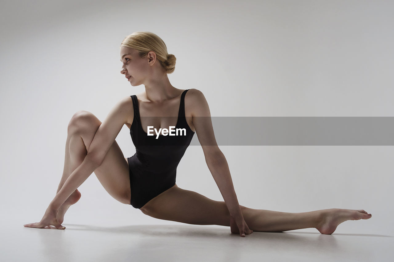 A ballerina sexually sits in a stretch with one knee raised and showing her foot