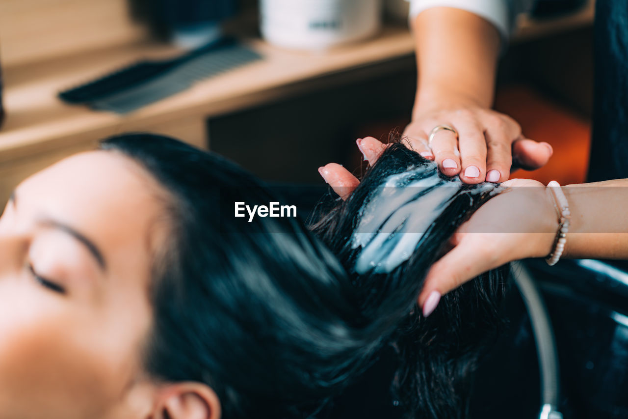 Cropped hands of hairdresser applying shampoo on woman hair in salon