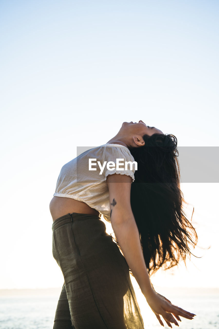 Young latina woman dancing by the ocean at golden hour in summertime