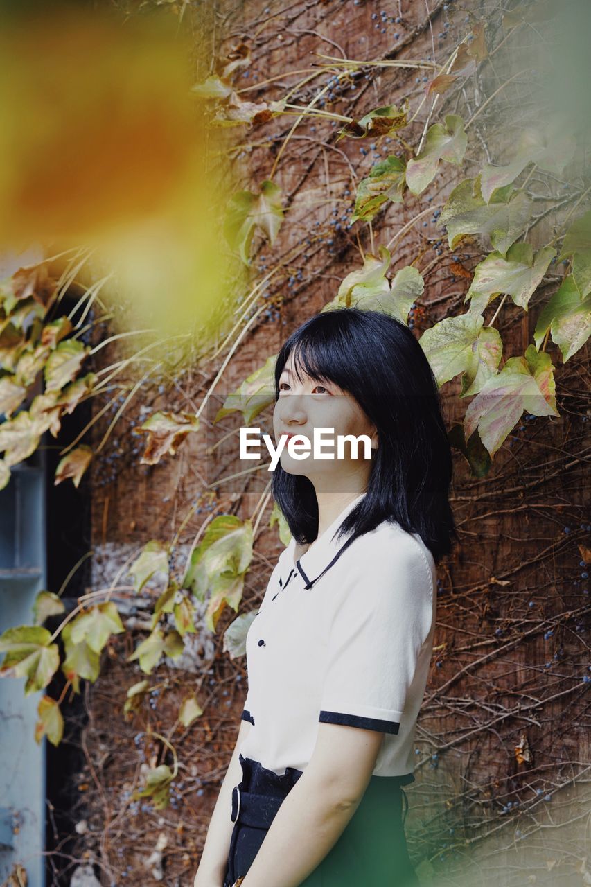 PORTRAIT OF BEAUTIFUL YOUNG WOMAN STANDING BY PLANTS