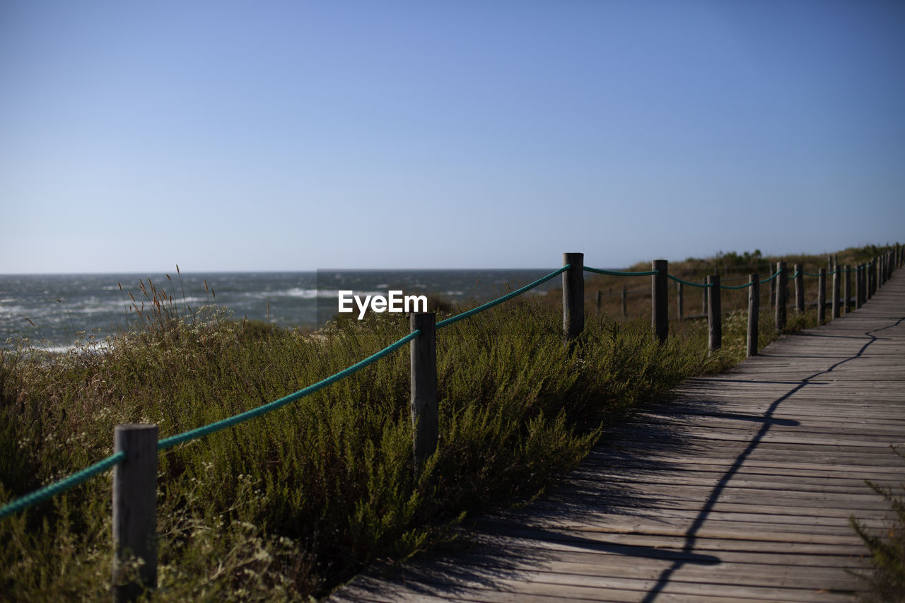 Footpath by sea against clear sky