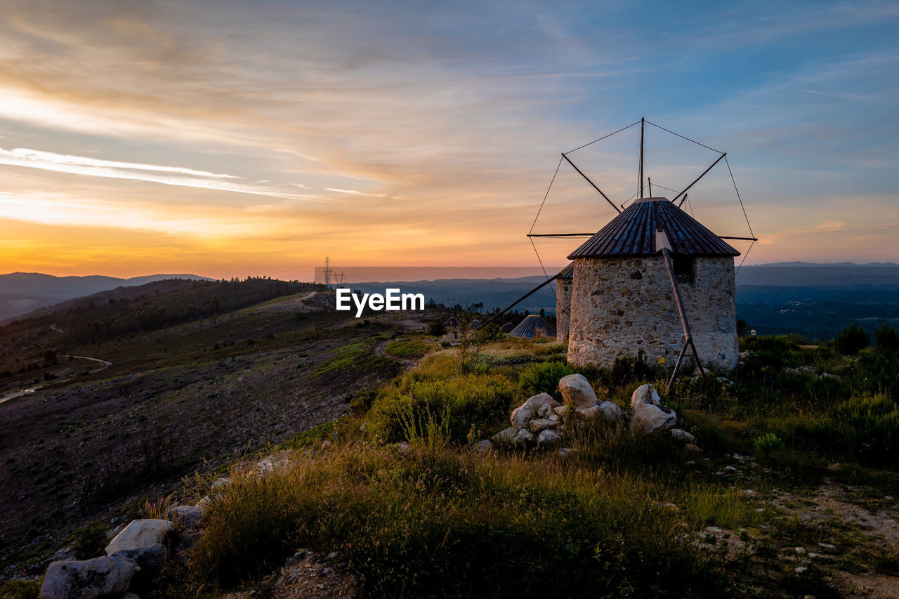 Small windmill on hill against cloudy sky during sunset