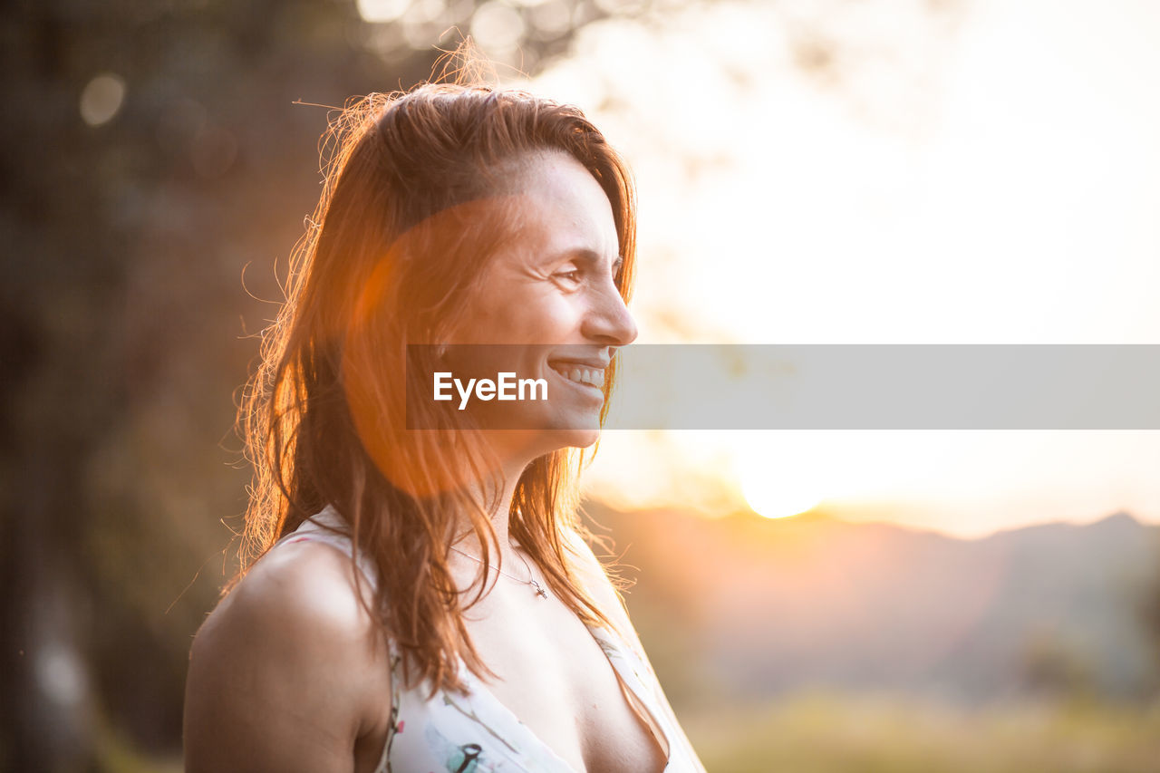 Smiling woman looking away against sky during sunset