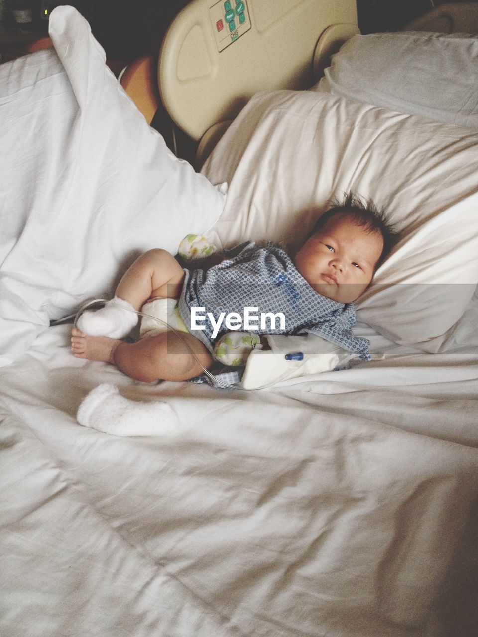 Portrait of cute baby boy with iv drip lying on bed at home