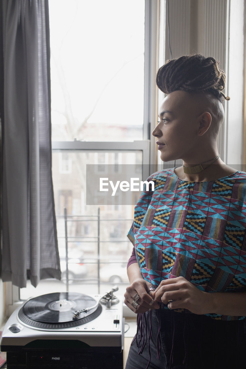 Thoughtful young woman standing by turntable at home