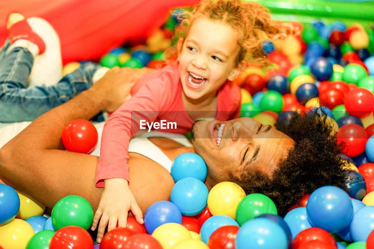 Happy father and daughter playing with multi colored balls in pool