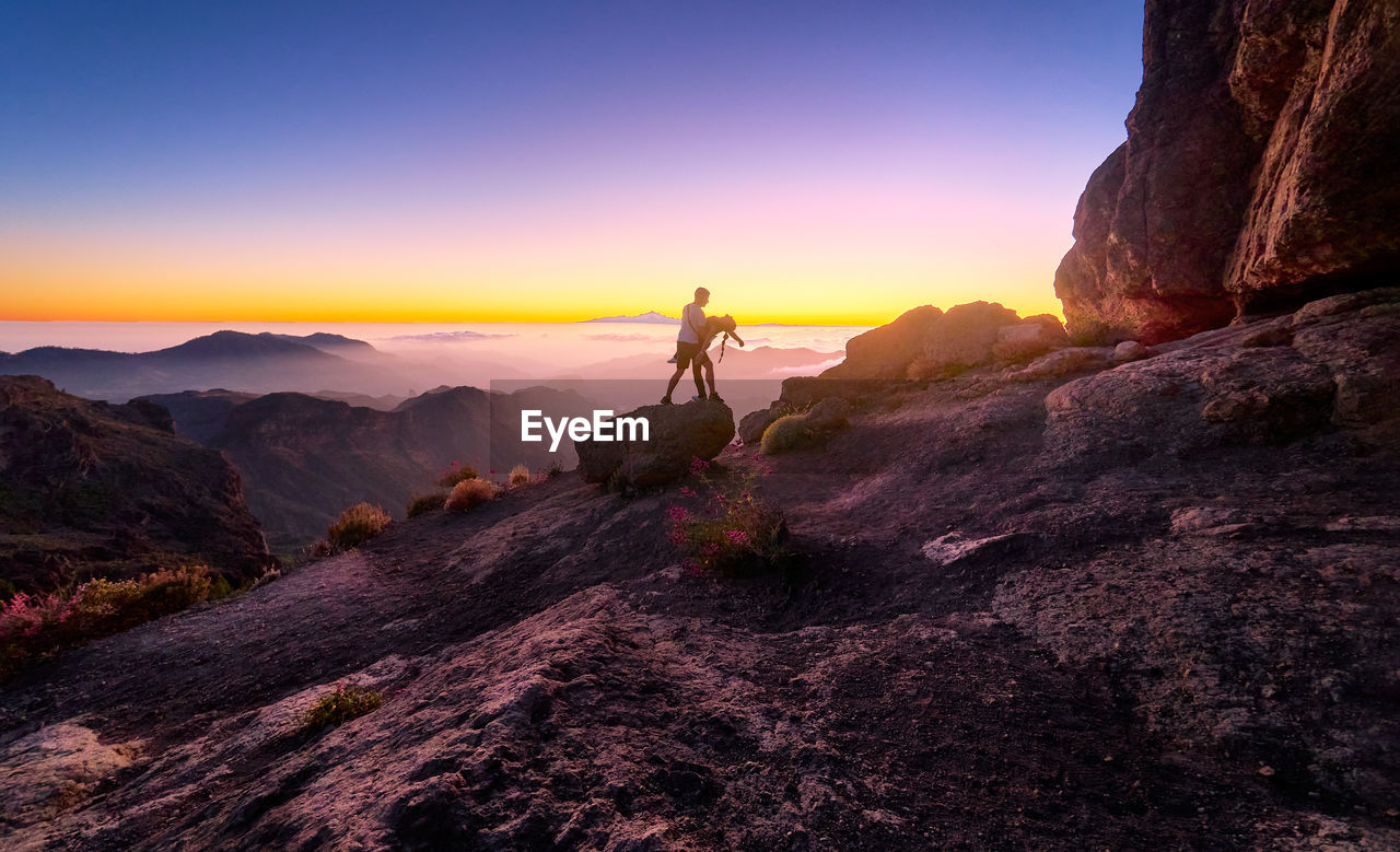 Man on rocks at mountain against sky during sunset