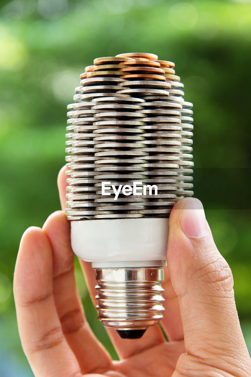 Close-up of hand holding light bulb with stack of coins