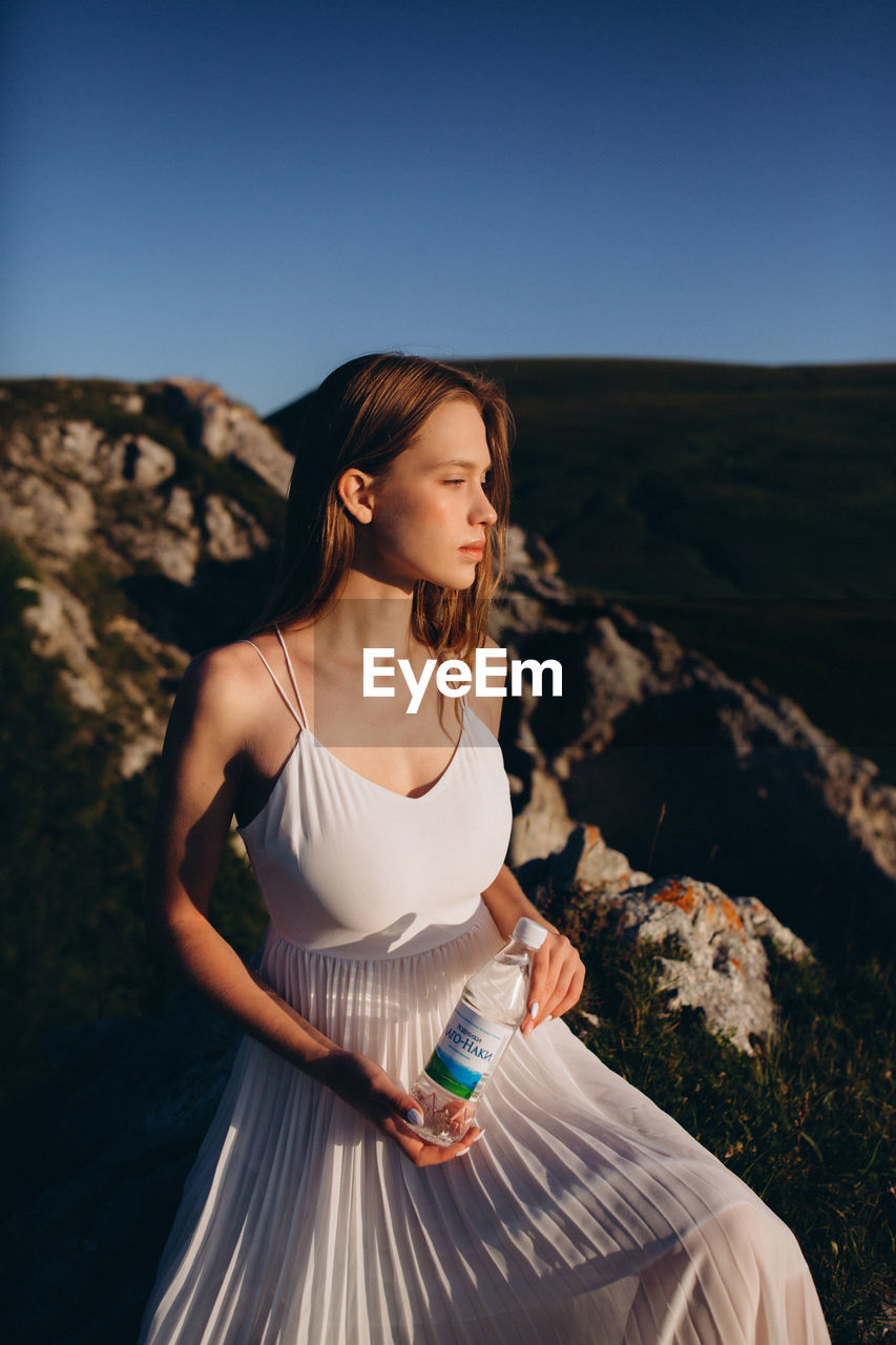 WOMAN LOOKING AWAY WHILE STANDING ON ROCK