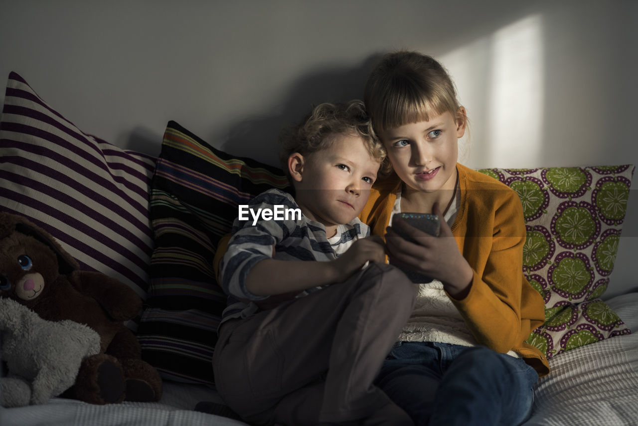 Siblings using mobile phone while sitting on sofa at home