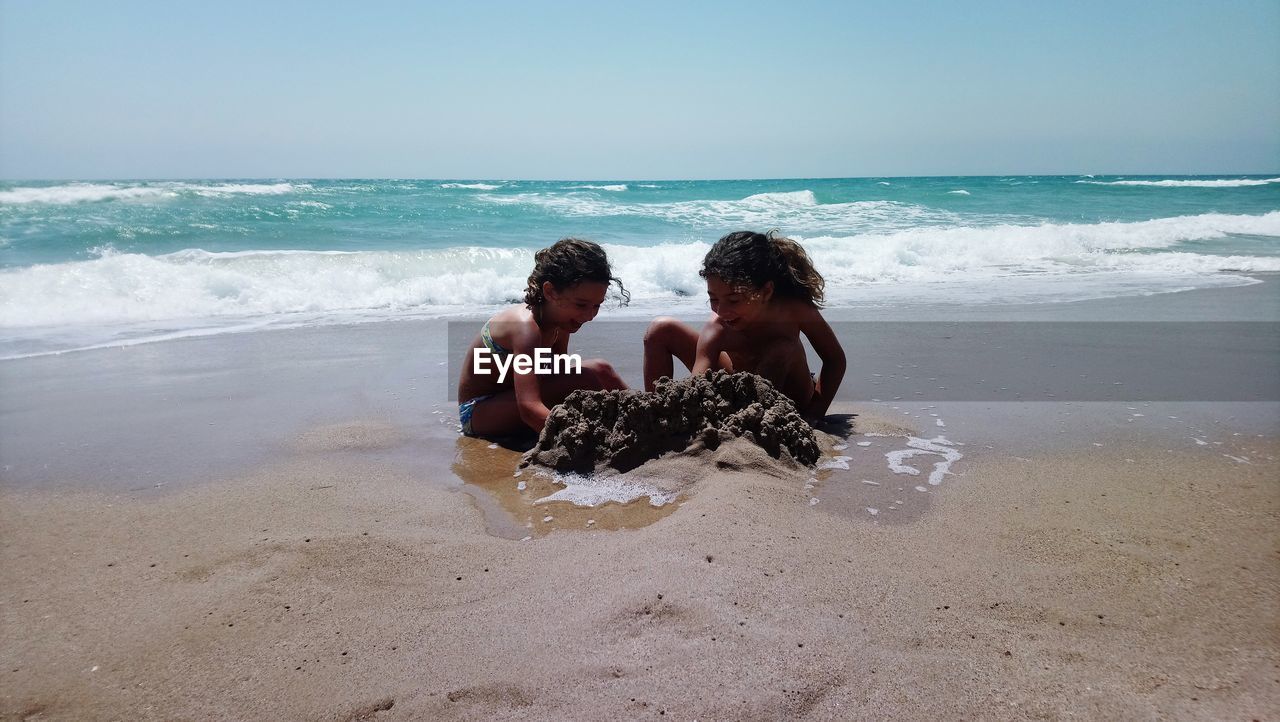 Friends playing with sand at beach against clear sky