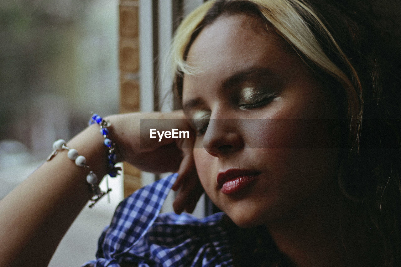 Close-up of young woman with eyes closed by window