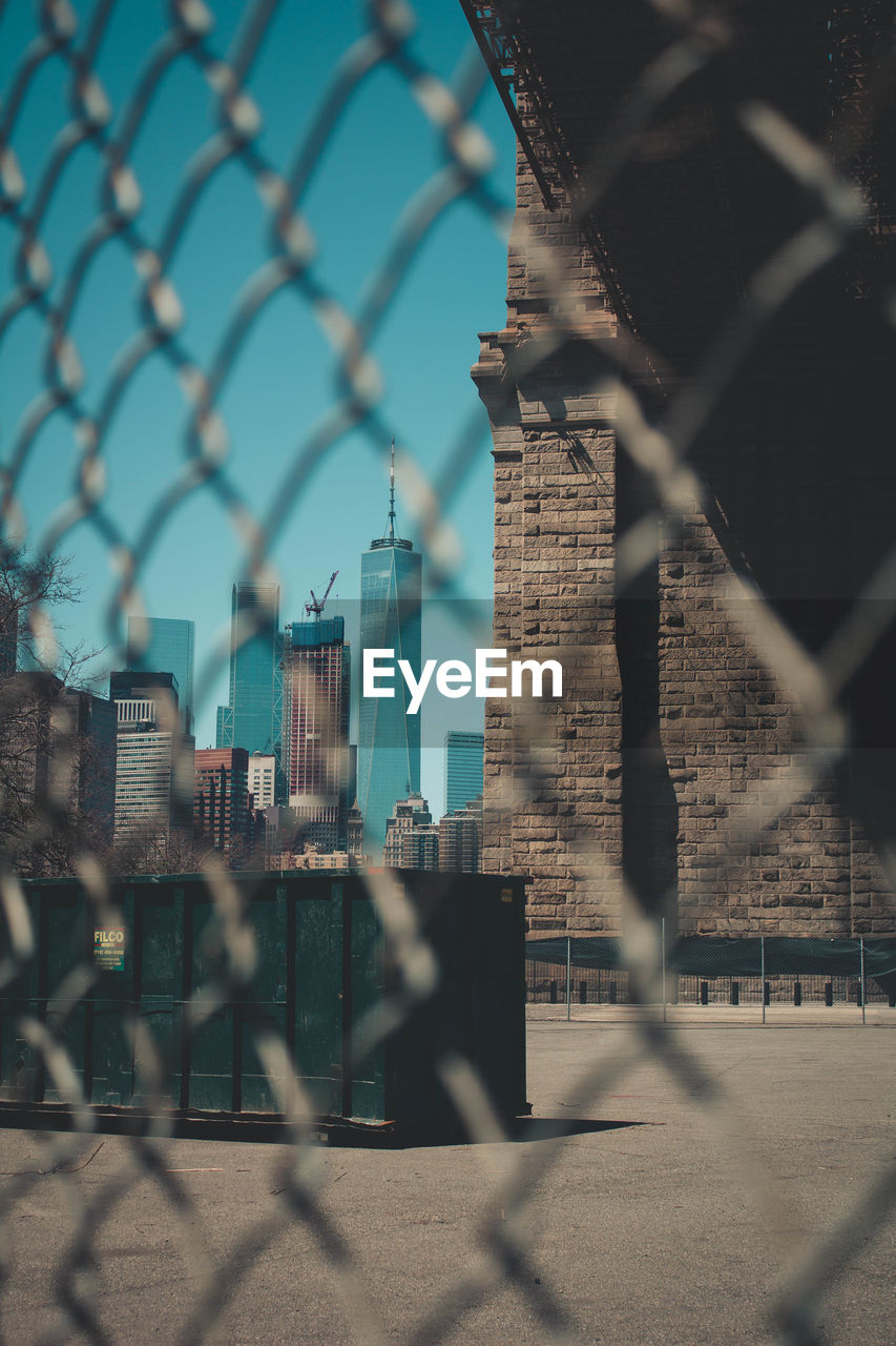 Cityscape seen through chainlink fence against sky