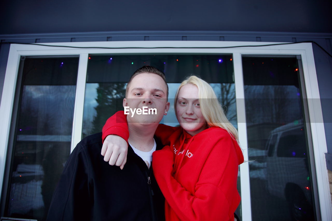 Portrait of smiling young siblings standing against house window