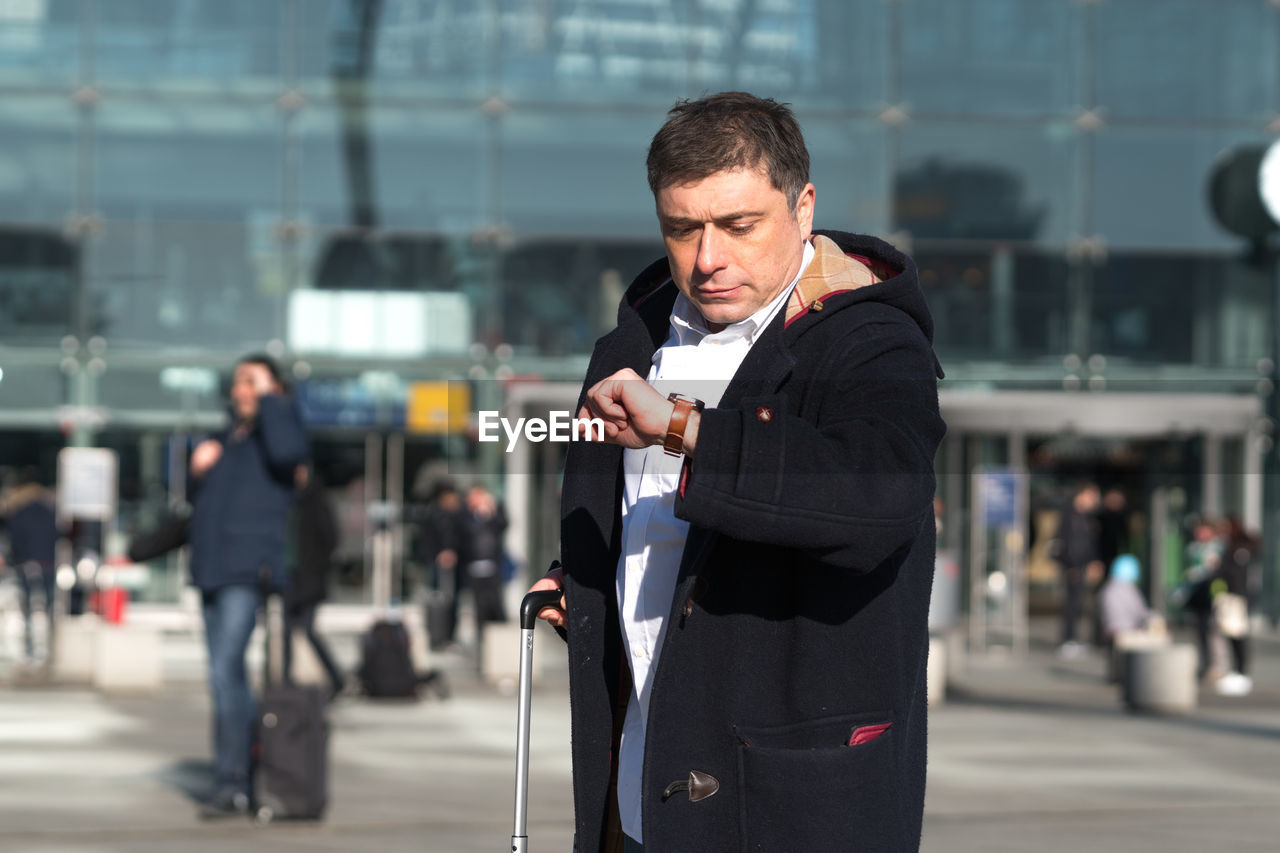 Man checking time while standing against building