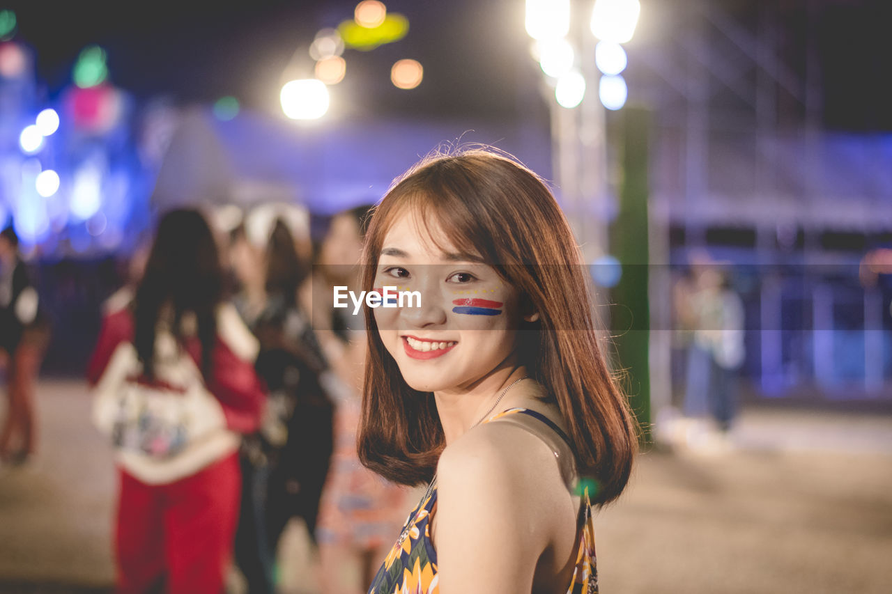 Portrait of smiling young woman standing outdoors at night