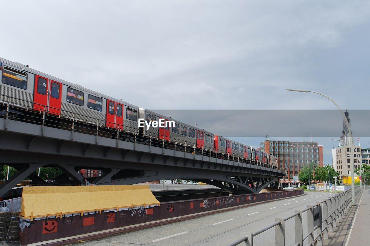 Low angle view of train moving on railway bridge in city against cloudy sky