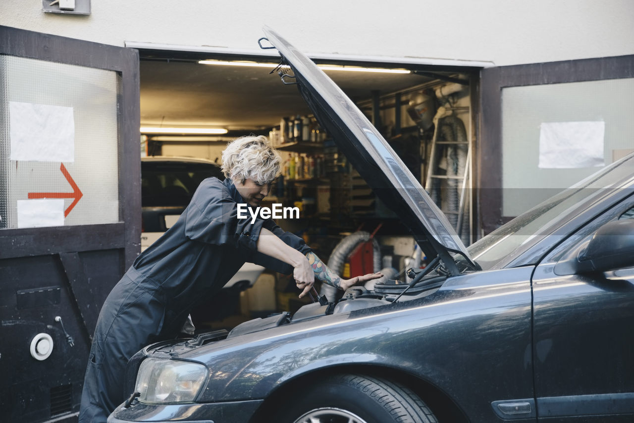 Side view of female mechanic repairing car outside auto repair shop