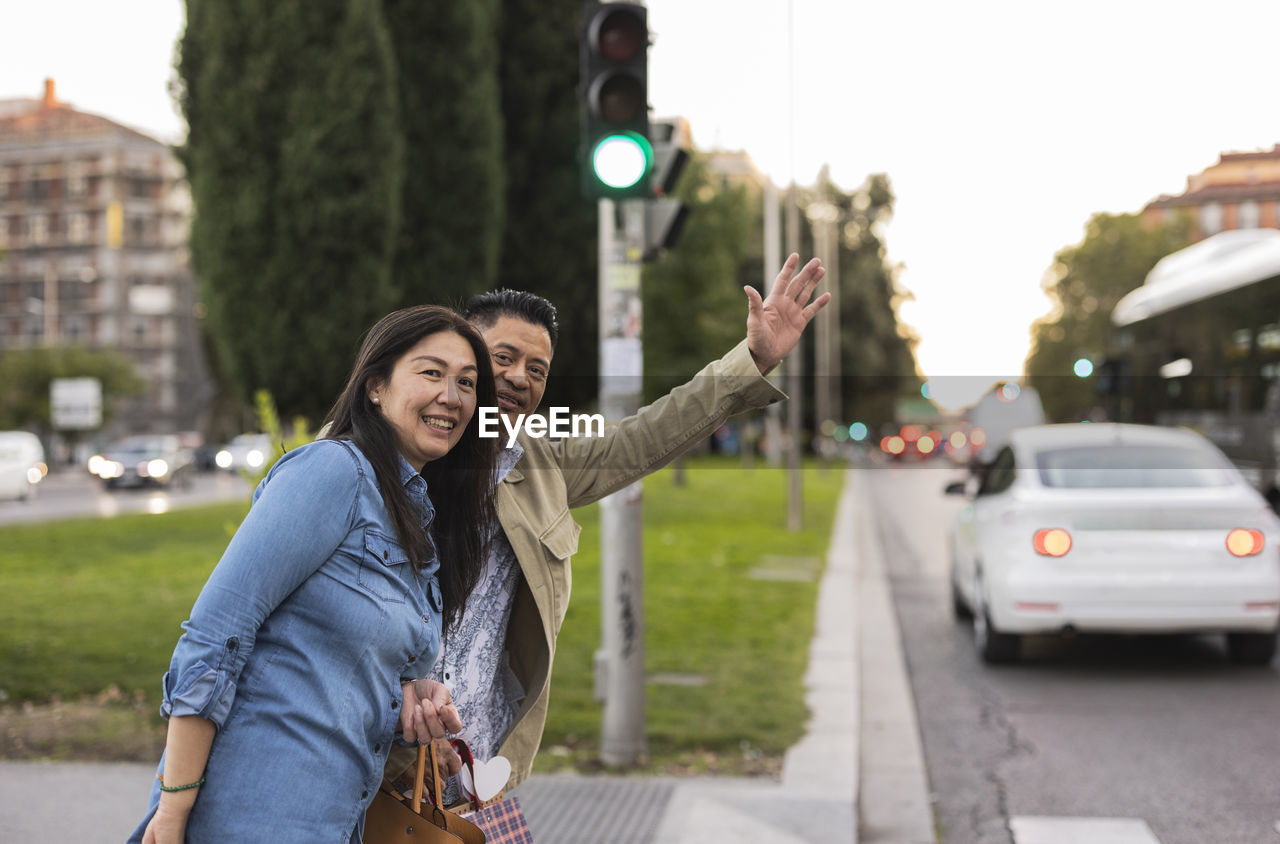 Smiling woman standing by man hailing footpath by street