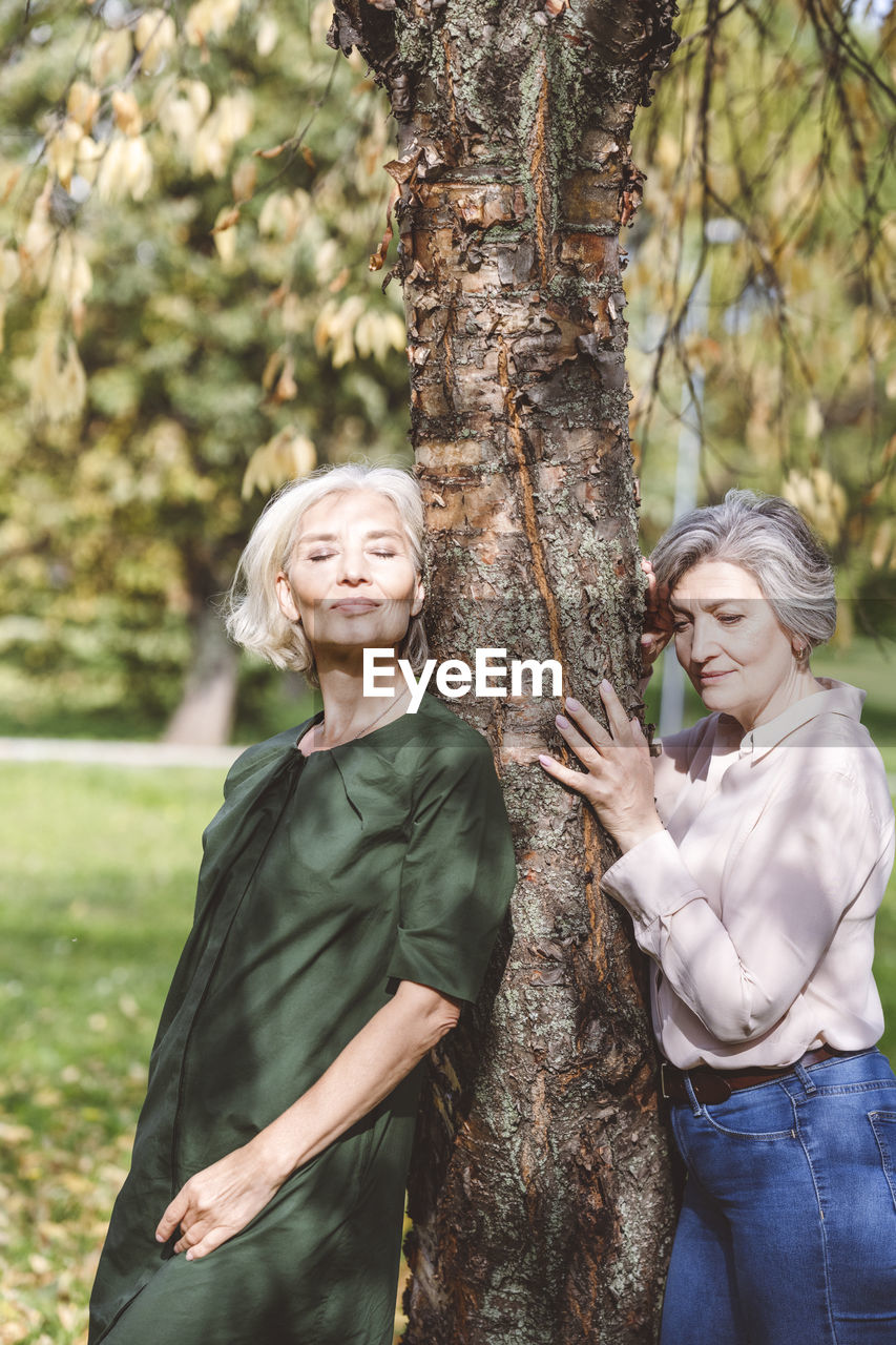 Friends leaning and embracing tree while standing at park