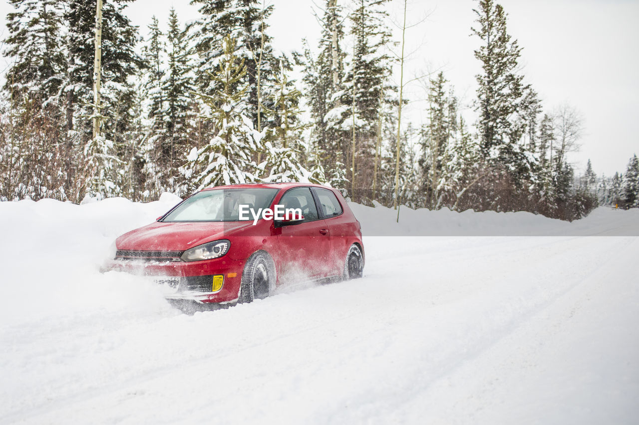 Side view of red car driving on snow covered road.