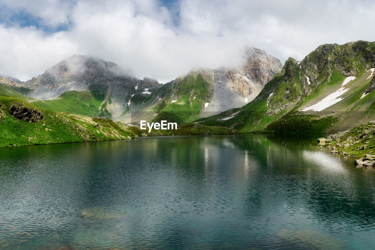 Mountain landscape with small glacial lake . mountain peaks with snow, green grass in the foreground