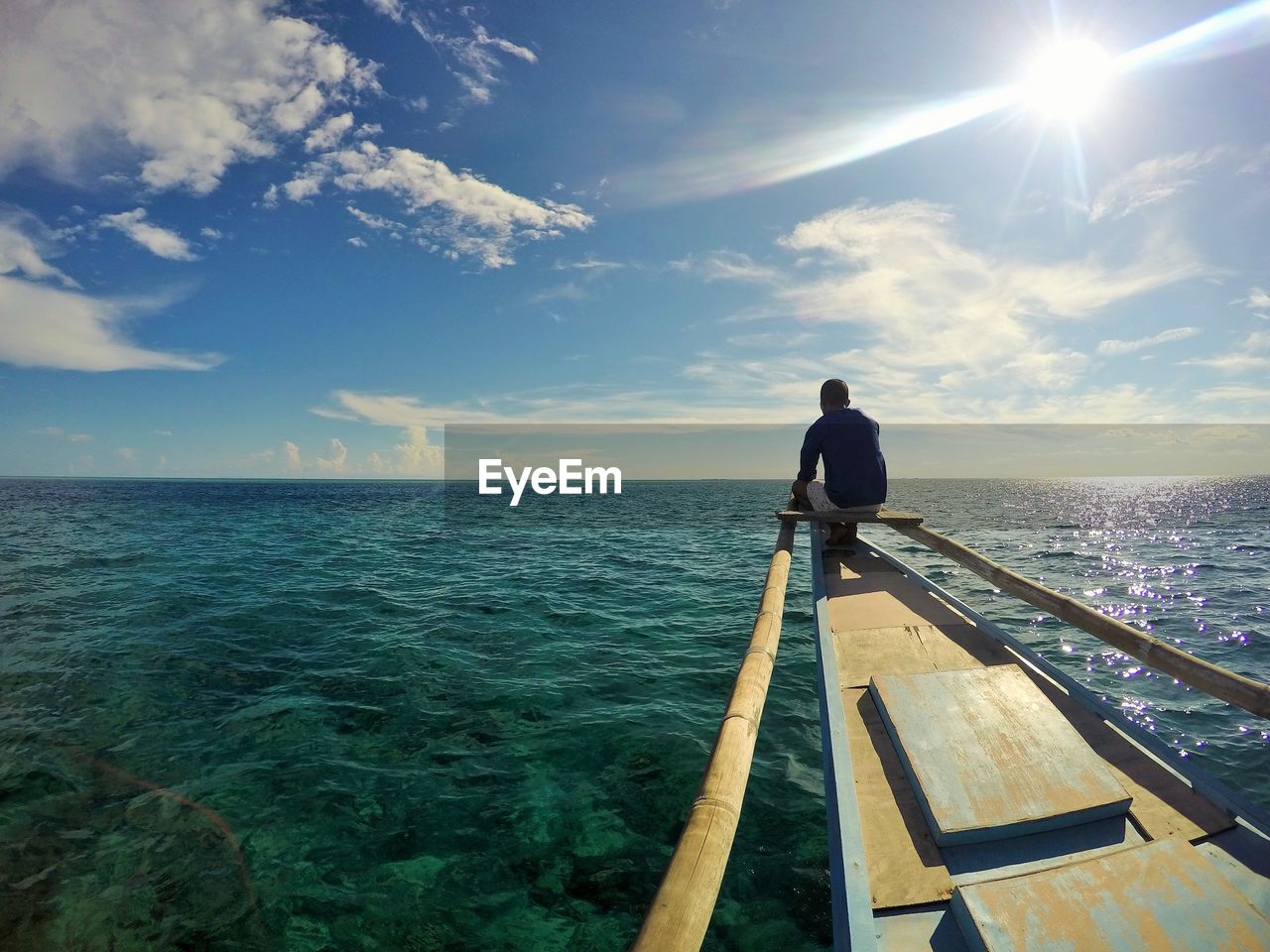 Rear view of man sitting on boat over sea against sky