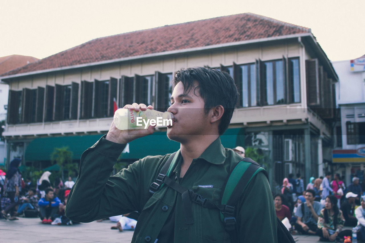 PORTRAIT OF YOUNG MAN DRINKING DRINK IN CITY