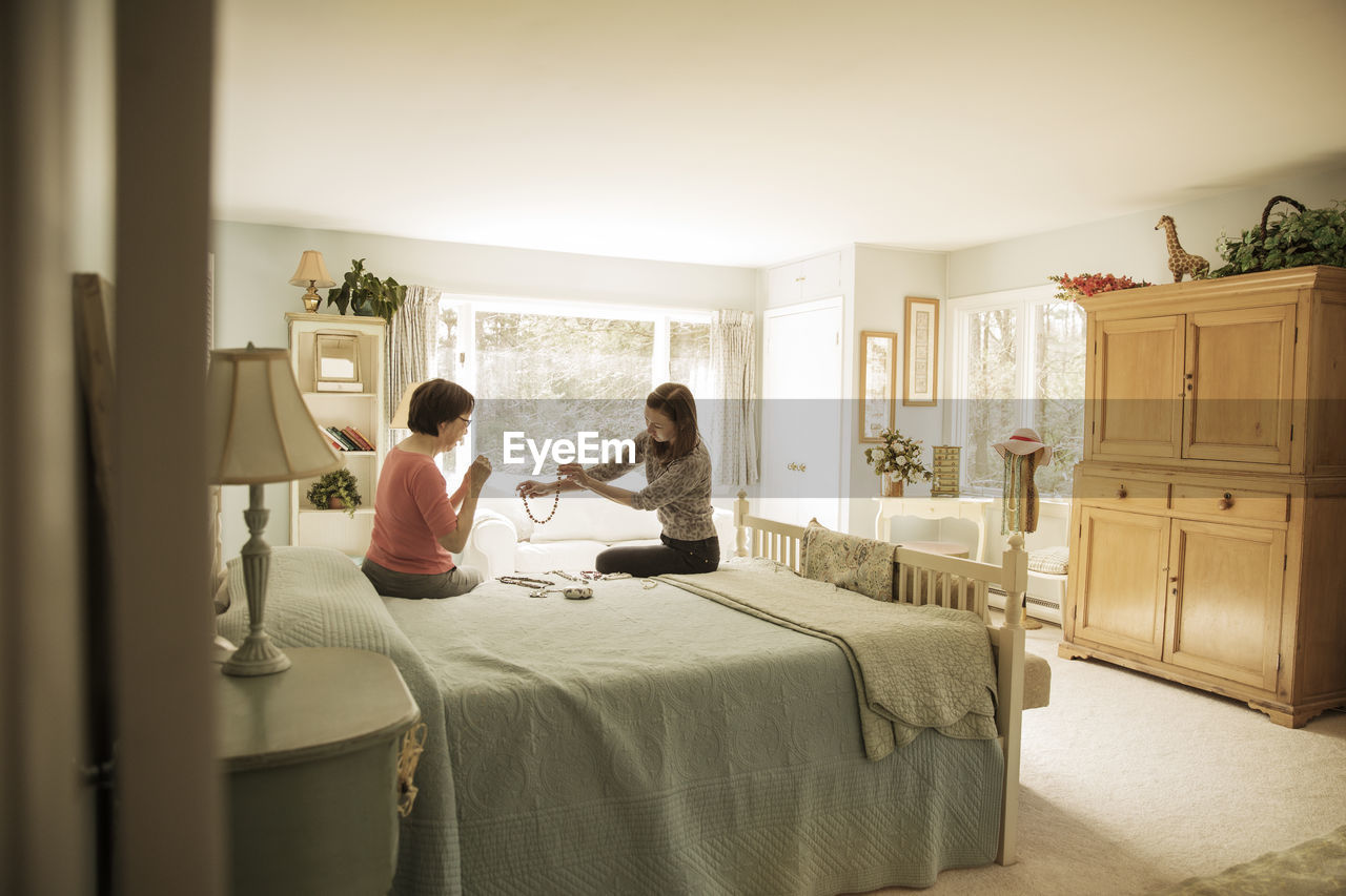 Mother and daughter looking at necklace while sitting on bed