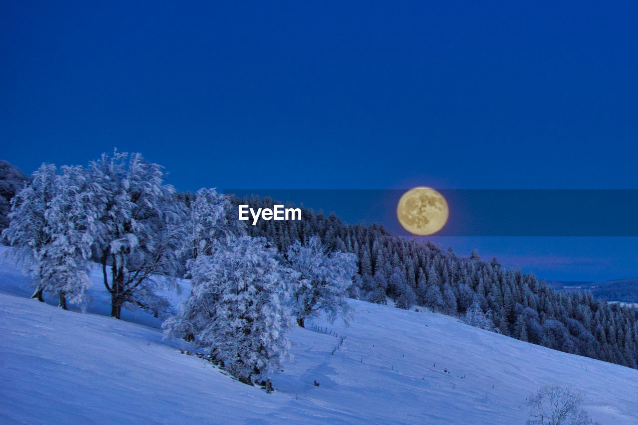 Scenic view of snow covered land against clear blue sky with full moon