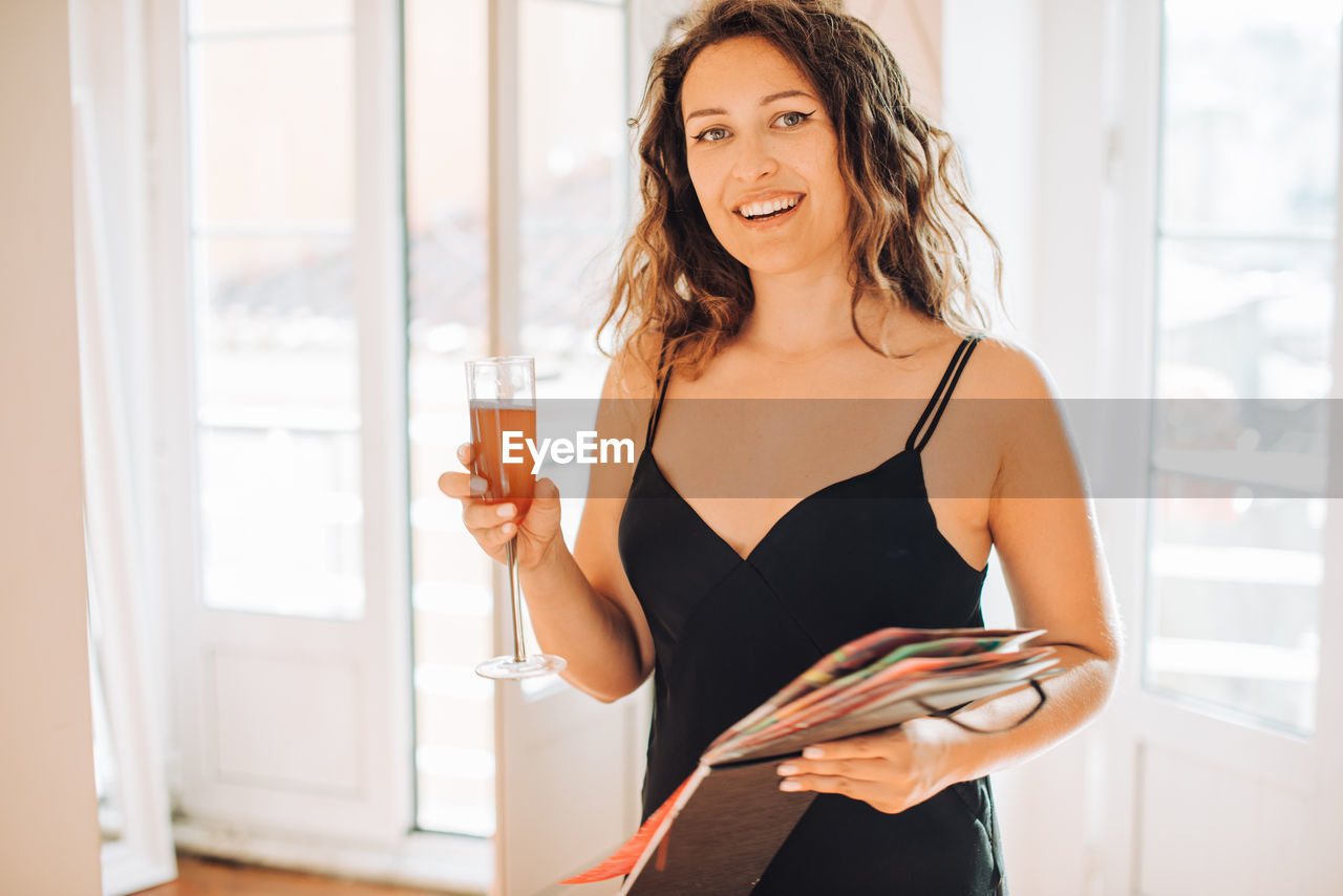 Woman in black dress holding glass of wine and album looking at camera