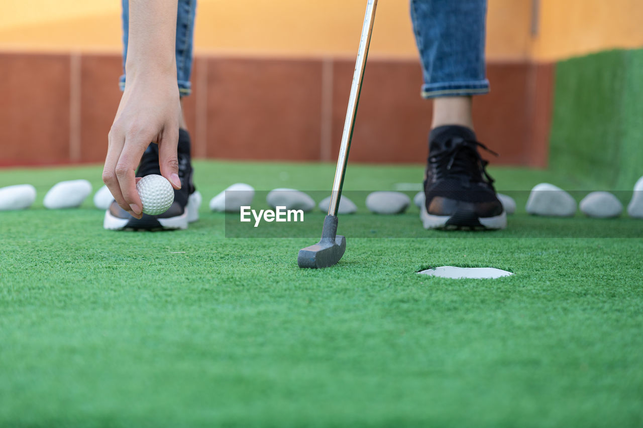 sports, golf, leisure activity, ball, activity, golf ball, golf course, low section, golf club, green, ball game, adult, weekend activities, grass, recreation, game, one person, miniature golf, human leg, men, green - golf course, lifestyles, standing, player, selective focus, relaxation, putting, day, golfer, putting green, shoe, hole, casual clothing, limb, individual sports, human limb, copy space, skill, sports equipment, outdoors, women