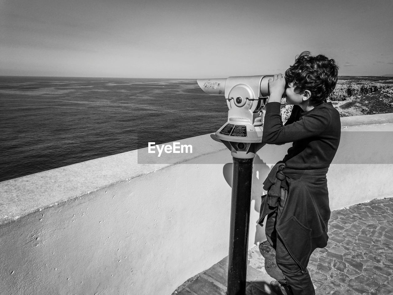 Boy looking at the sea through binoculars, in sagres, portugal.