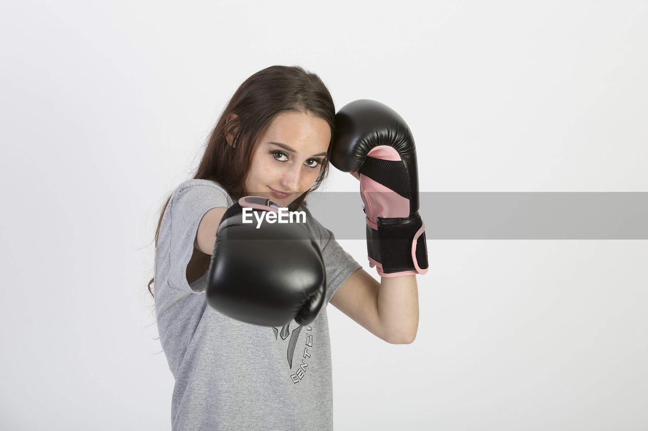 one person, adult, boxing, exercising, women, sports training, boxing glove, sports, studio shot, indoors, strength, lifestyles, arm, athlete, young adult, portrait, headphones, sports clothing, copy space, limb, vitality, waist up, clothing, white background, listening, photo shoot, sports glove, muscular build, standing, hairstyle, female, gym, brown hair, punching, gray, front view, long hair, cut out